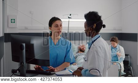 Medical Asisstant Typing Disease Symptom While Specialist Practitioner Doctors Monitoring Sick Man W