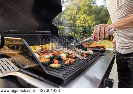 People Grilling Fish And Corn On A Modern Grill Outdoors At Sunet, Close-up. Cooking Food On The Ope