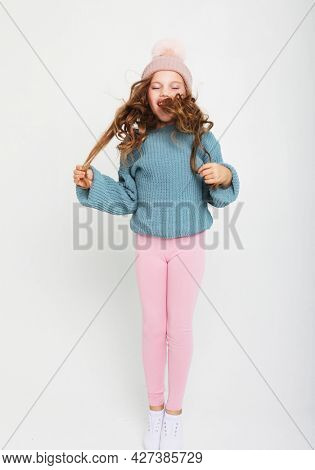 funny child girl with curly haor dressed blue sweater and winter hat jumping on white background