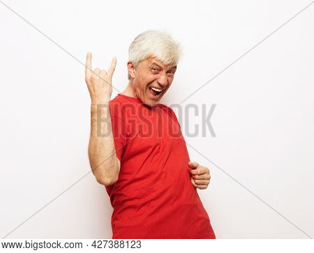 Senior man with white hair wearing red t-shirt shouting with crazy expression doing rock symbol with hands up.