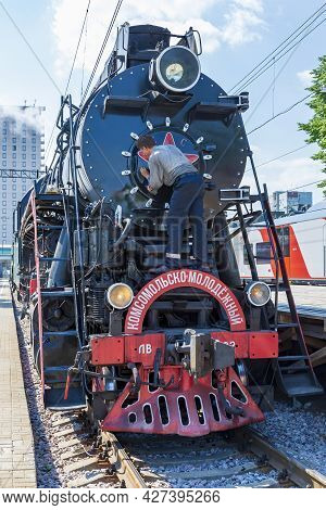 Worker Washes A Black Retro Steam Locomotive At The Railway Station