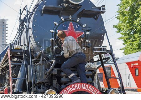Worker Washes A Black Retro Steam Locomotive At The Railway Station