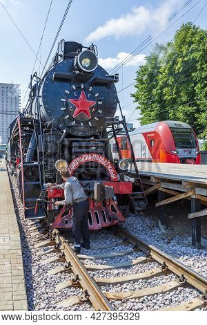 Worker Washes A Black Retro Steam Locomotive At The Railway Station