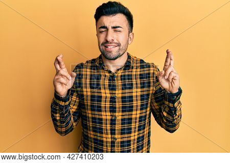 Young hispanic man wearing casual clothes gesturing finger crossed smiling with hope and eyes closed. luck and superstitious concept. 