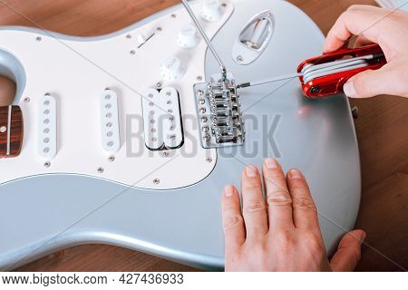 Guitar Master Adjusting Bridge Saddle On Tremolo Of Electric Guitar Using Multitool, Close Up Shot O