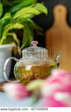 Green Tea With Rose Petals In A Transparent Teapot On A Wooden Table On A Black Background. The Back