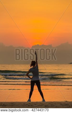 Good Shape Woman Standing And Exercise On Beanch In The Morning With Colorful Sky In Background.