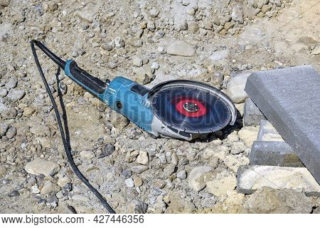 Electric Tool With Diamond Disc For Cutting Stones Lies On Gravel. Angle Grinder Is Ready For Operat