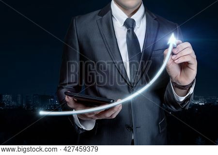 Business Man Draws A Sharp Rise In The Form Of An Arrow On A Blurred Background.