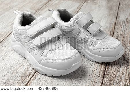 White Leather Sneakers On Light Background. A Pair Of Fashionable Childrens Sports Sneakers With A V