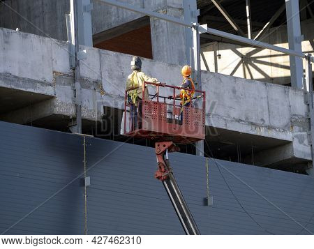 An Aerial Platform Lifts Workers To The Upper Floors Of A Building Under Construction. Background Wi