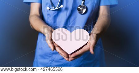 Young Woman Doctor, A Cardiologist Gently Holds A Pink Heart In Her Hands. The Nurse Treats Patients