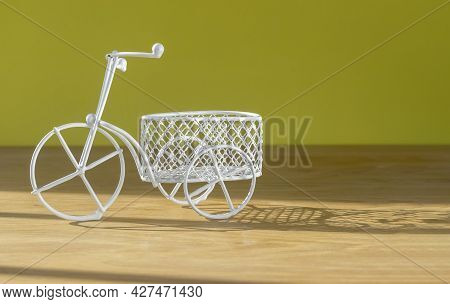 Cute Retro Bicycle Toy With Basket On Wooden Desk With Sun Light Over Yellow Wall With Copy Space Fo
