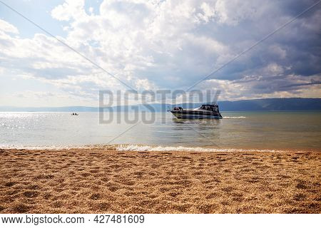 Yacht With Tourists In A Beautiful Bay On Lake Baikal. Cloudy Sky, Sandy Beach With Small Pebbles. S