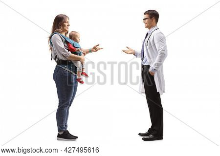 Full length profile shot of a doctor and a mother with a baby in a carrier having a conversation isolated on white background