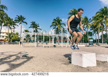 Training squat jumping on box in outdoor beach gym. Man athlete workout at Fitness bench jumping at Miami Beach . Strength training exercise fit male working out outdoors.
