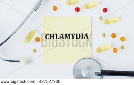 Card With The Text Chlamydia On A White Background Next To Scattered Pills And A Stethoscope