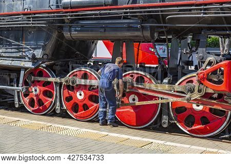 Worker Checks A Black Retro Steam Locomotive At Railway Station