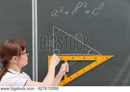 School Teacher Young Woman In The Class At The Blackboard Draws A Triangle With A Ruler. Portrait. C