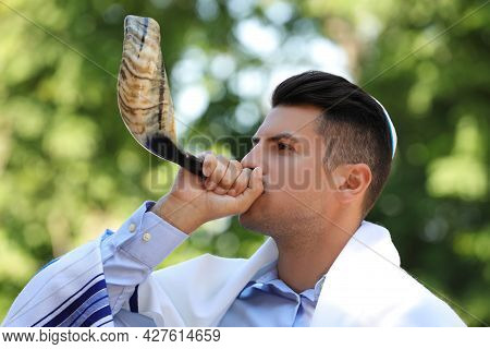 Jewish Man In Kippah And Tallit Blowing Shofar Outdoors. Rosh Hashanah Celebration