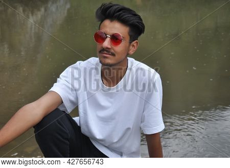 A Good Looking Young Guy Sitting Beside Of River With Resting His Hand On His Knee With Looking Side