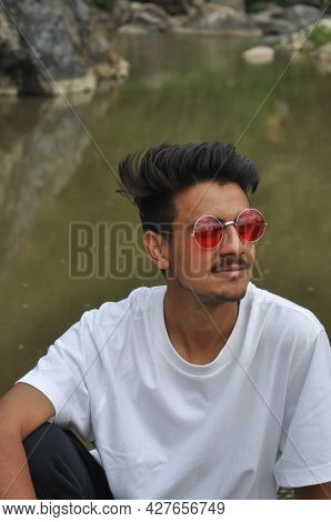 A Good Looking Young Guy Sitting Beside Of River With Resting His Hand On His Knee With Looking Side