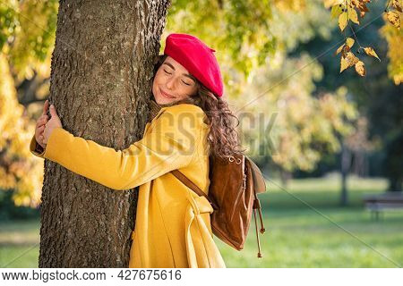 Smiling girl with closed eyes hugging tree at park during autumn season. Beautiful woman hugging a tree. woman embracing a tree trunk with a blissful expression: environmental conservation.