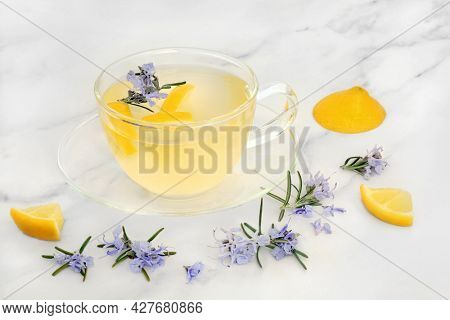 Immune system boosting rosemary and lemon herbal tea in a glass cup on marble. High in antioxidants and vitamin c. Can also be used for cold and flu virus remedy and to ease digestive problems.