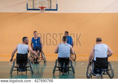 Disabled War veterans mixed race opposing basketball teams in wheelchairs photographed in action while playing an important match in a modern hall. 