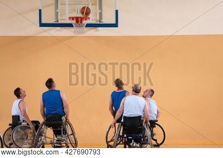 Disabled War veterans mixed race opposing basketball teams in wheelchairs photographed in action while playing an important match in a modern hall. 