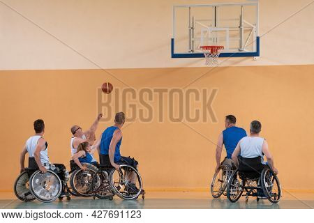 Disabled War veterans mixed race opposing basketball teams in wheelchairs photographed in action while playing an important match in a modern hall. 
