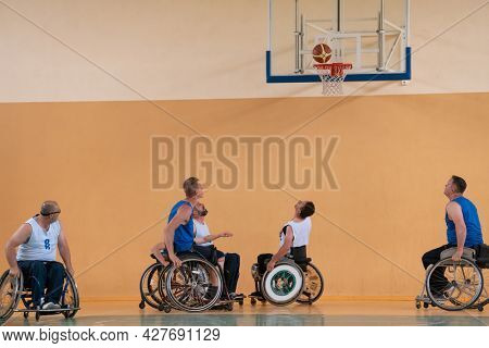 Disabled War veterans mixed race opposing basketball teams in wheelchairs photographed in action while playing an important match in a modern hall. 