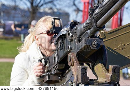 A Blonde Woman In Dark Glasses Shoots An Anti-aircraft Machine Gun Aiming Upwards. War And Terror Co