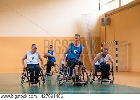 Disabled War veterans mixed race opposing basketball teams in wheelchairs photographed in action while playing an important match in a modern hall. 