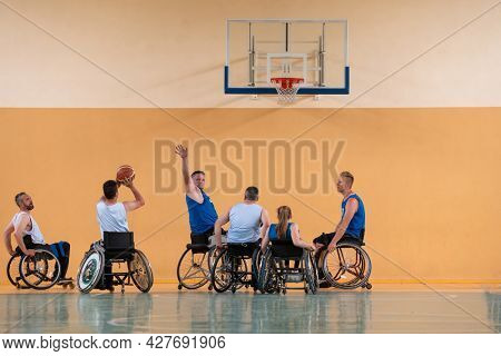 Disabled War veterans mixed race opposing basketball teams in wheelchairs photographed in action while playing an important match in a modern hall. 
