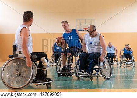 Disabled War veterans mixed race opposing basketball teams in wheelchairs photographed in action while playing an important match in a modern hall. 