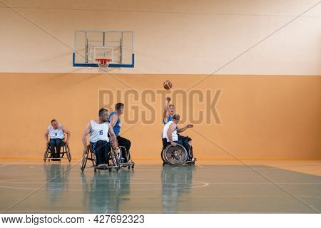 Disabled War veterans mixed race opposing basketball teams in wheelchairs photographed in action while playing an important match in a modern hall. 