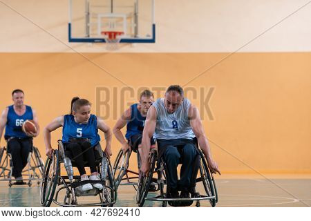 Disabled War veterans mixed race opposing basketball teams in wheelchairs photographed in action while playing an important match in a modern hall. 