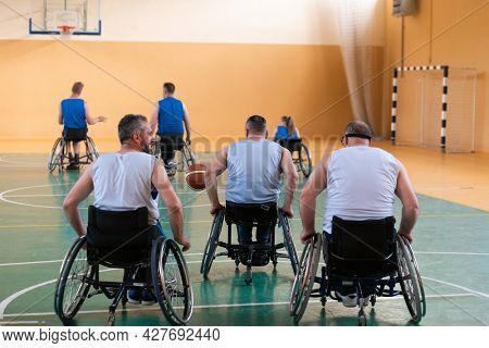 Disabled War veterans mixed race opposing basketball teams in wheelchairs photographed in action while playing an important match in a modern hall. 
