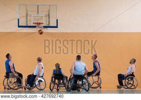 Disabled War veterans mixed race opposing basketball teams in wheelchairs photographed in action while playing an important match in a modern hall. 