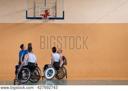 Disabled War veterans mixed race opposing basketball teams in wheelchairs photographed in action while playing an important match in a modern hall. 