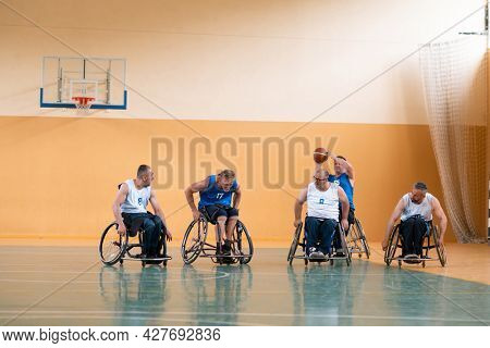 Disabled War veterans mixed race opposing basketball teams in wheelchairs photographed in action while playing an important match in a modern hall. 