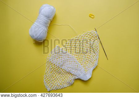 The Process Of Creating A String Bag. A White String Bag, A Knitting Hook And A Skein Of Yarn On A Y