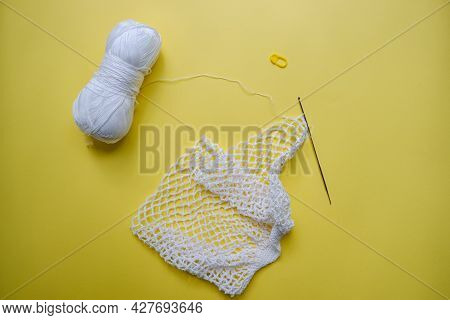 The Process Of Creating A String Bag. A White String Bag, A Knitting Hook And A Skein Of Yarn On A Y