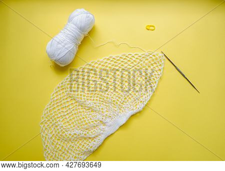 The Process Of Creating A String Bag. A White String Bag, A Knitting Hook And A Skein Of Yarn On A Y