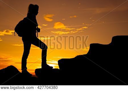 Woman Walking On Top Of Mountain At Twilight With Backpack