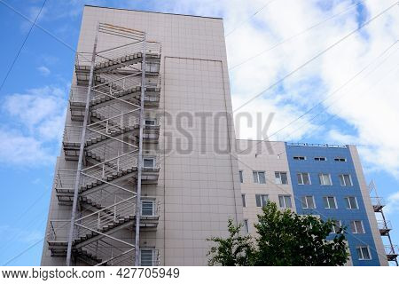 Modern Residential Building With A Fire Escape Against A Blue Sky With Clouds. Fire Escape Stairs On