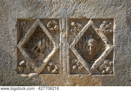 Ancient Lycian stone slab with human portrait and bird carved in stone in geometric form with floral decoration, Ruins of ancient city of Myra in Demre, Turkey