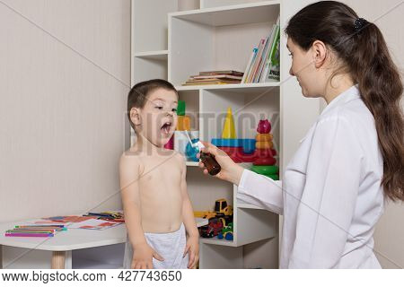A Pediatrician Or Nurse And A Boy 3-4 Years Old. Throat Spray, Treatment Of Pharyngitis, Stomatitis 