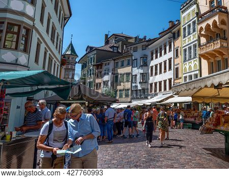 Bolzano, Italy, June 2021. At The Local Market Two Tourists Are Consulting The Tourist Map. One Poin